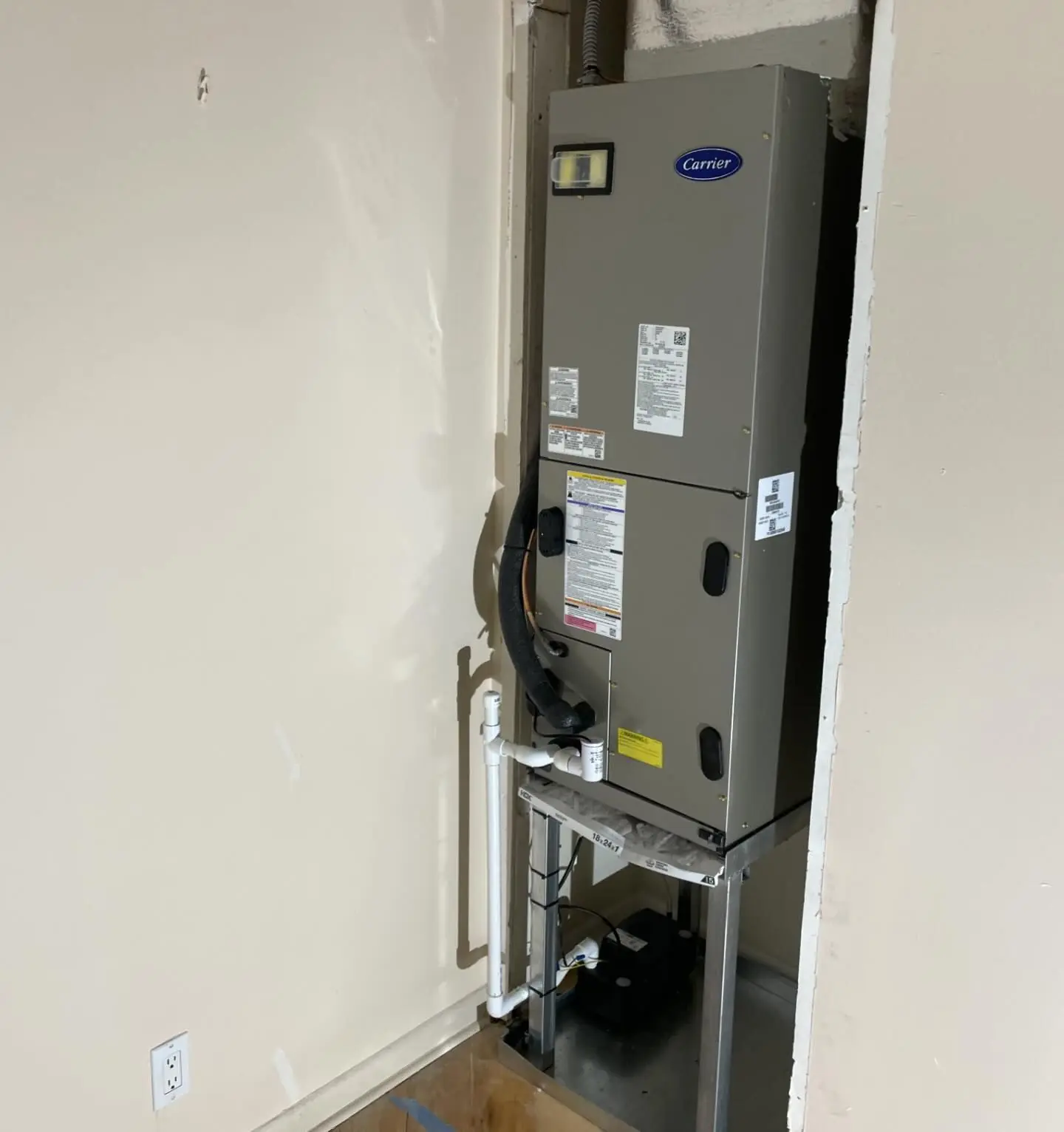 New Carrier air handler on a metal stand in a utility closet, with the condensate drain line and a condensate pump below it