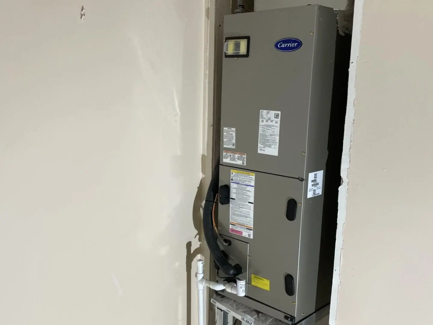 New Carrier air handler on a metal stand in a utility closet, with the condensate drain line and a condensate pump below it