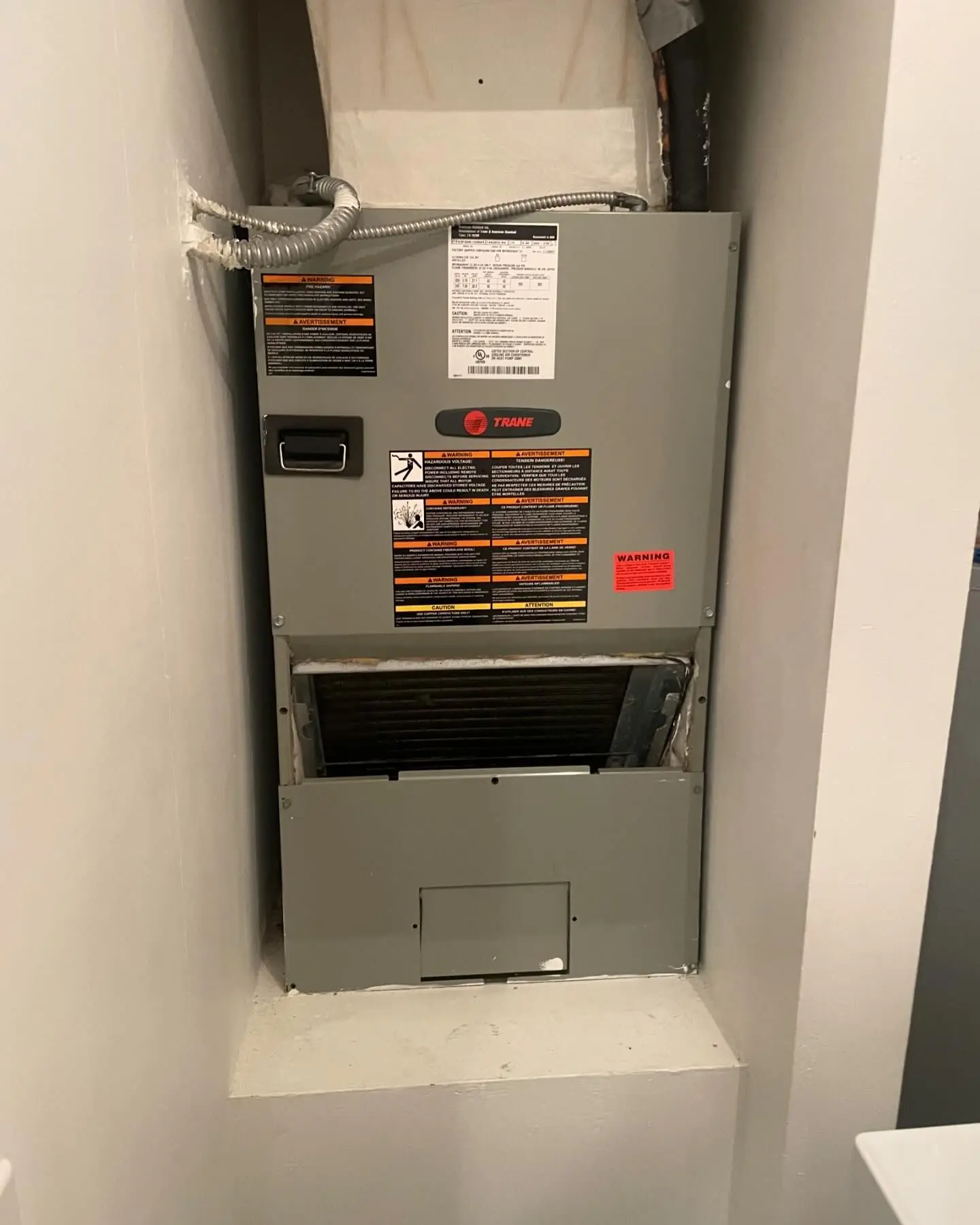Trane air handler installed in a wall closet, with the filter access door open below the cabinet