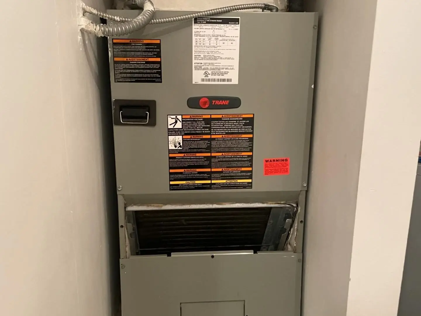 Trane air handler installed in a wall closet, with the filter access door open below the cabinet