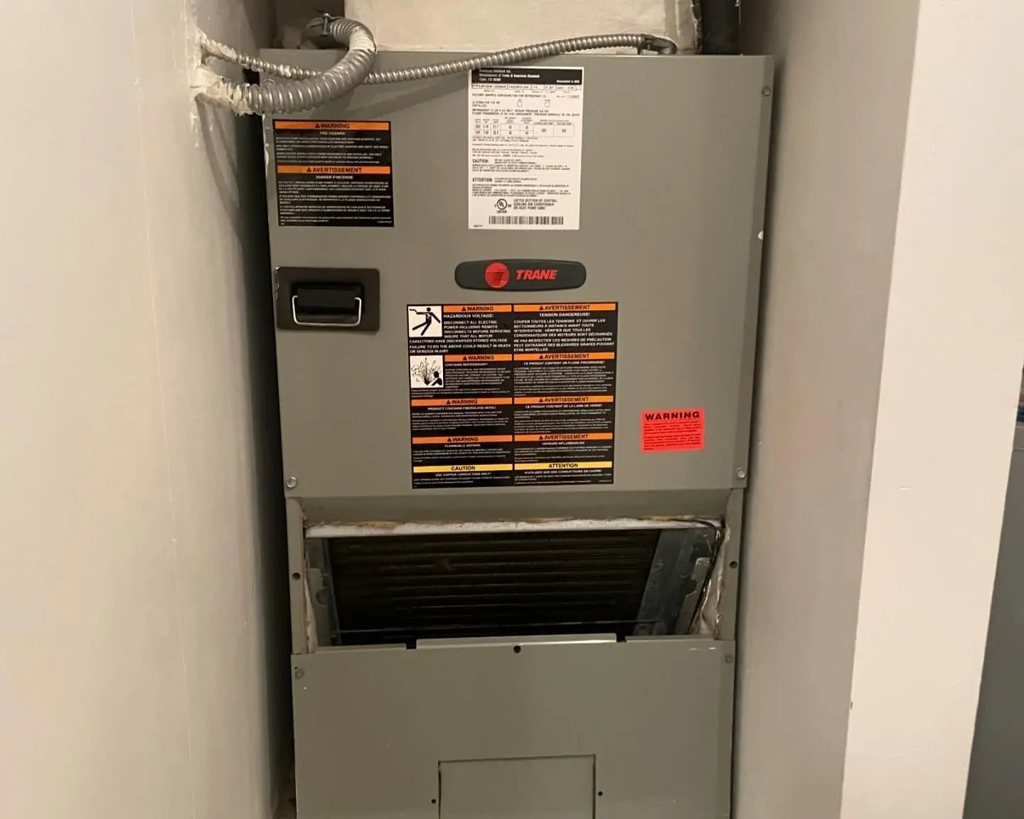 Trane air handler installed in a wall closet, with the filter access door open below the cabinet