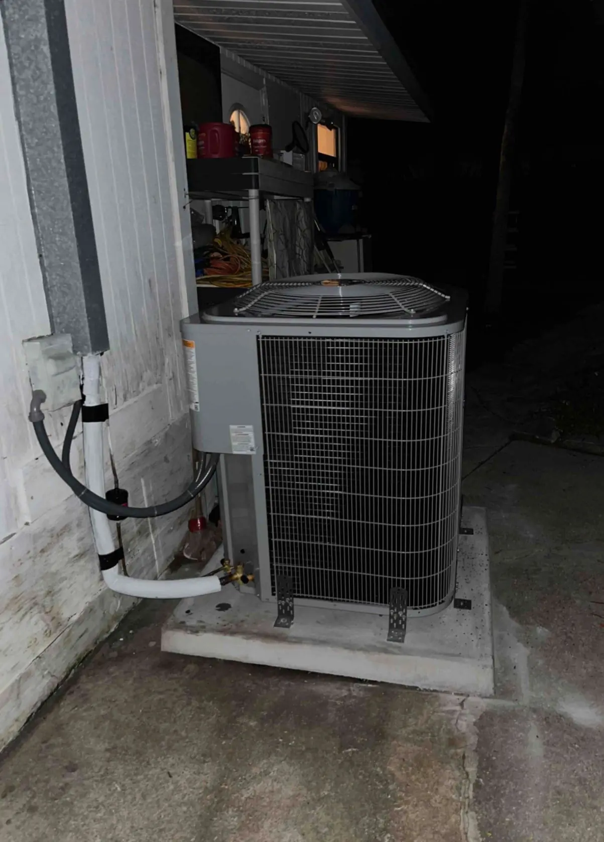 Newly installed outdoor condenser on a concrete pad beside a house, photographed at night