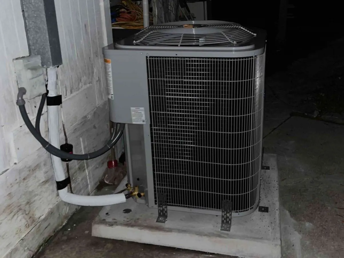 Newly installed outdoor condenser on a concrete pad beside a house, photographed at night