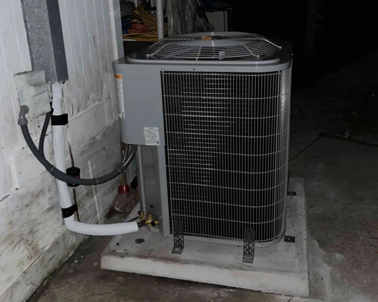Newly installed outdoor condenser on a concrete pad beside a house, photographed at night