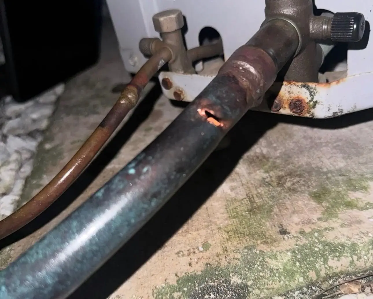 Corroded copper refrigerant line with a pinhole near the outdoor unit's service valve