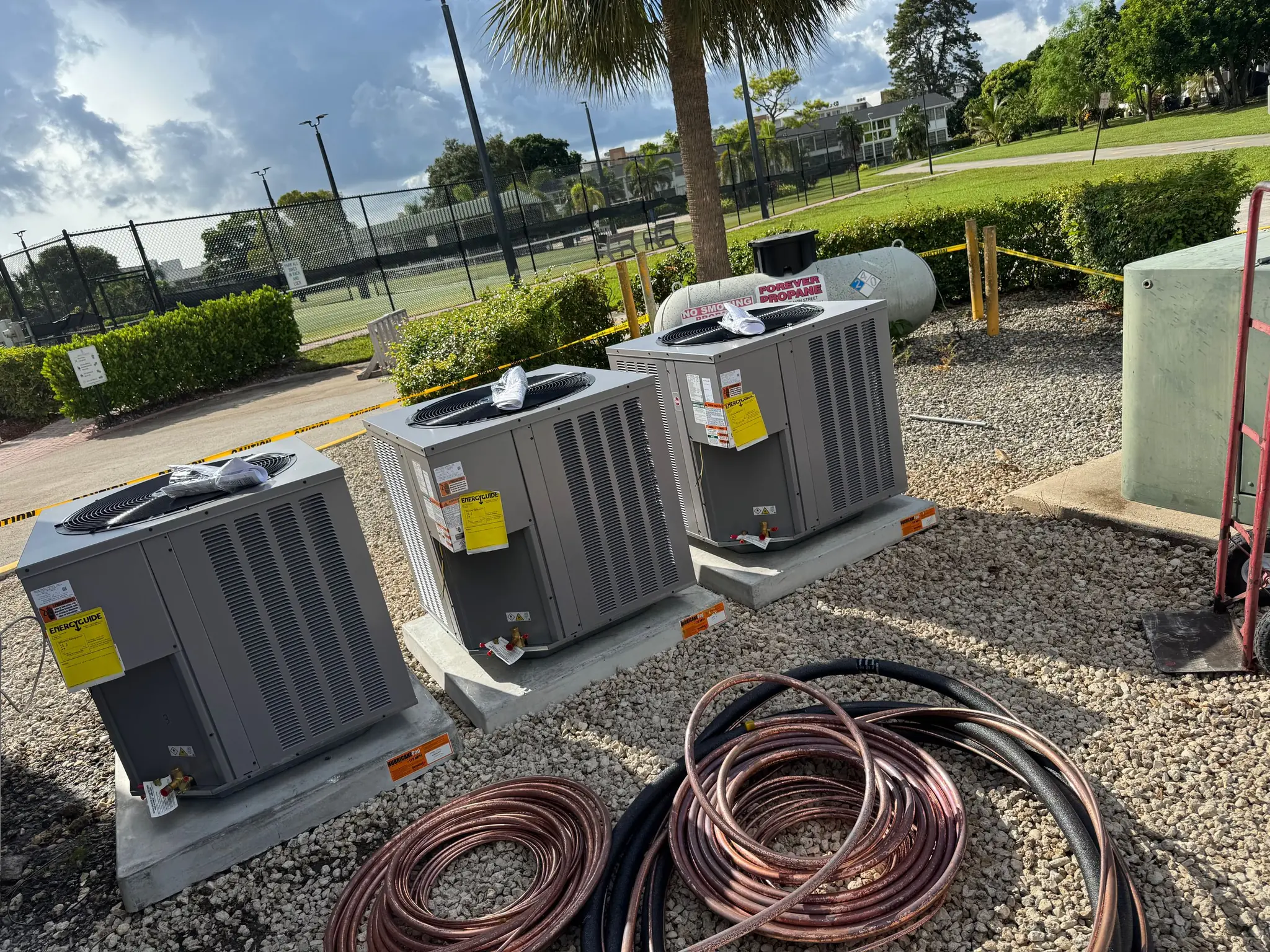 Three new outdoor condensing units set on pads, with coils of refrigerant line set ready to connect