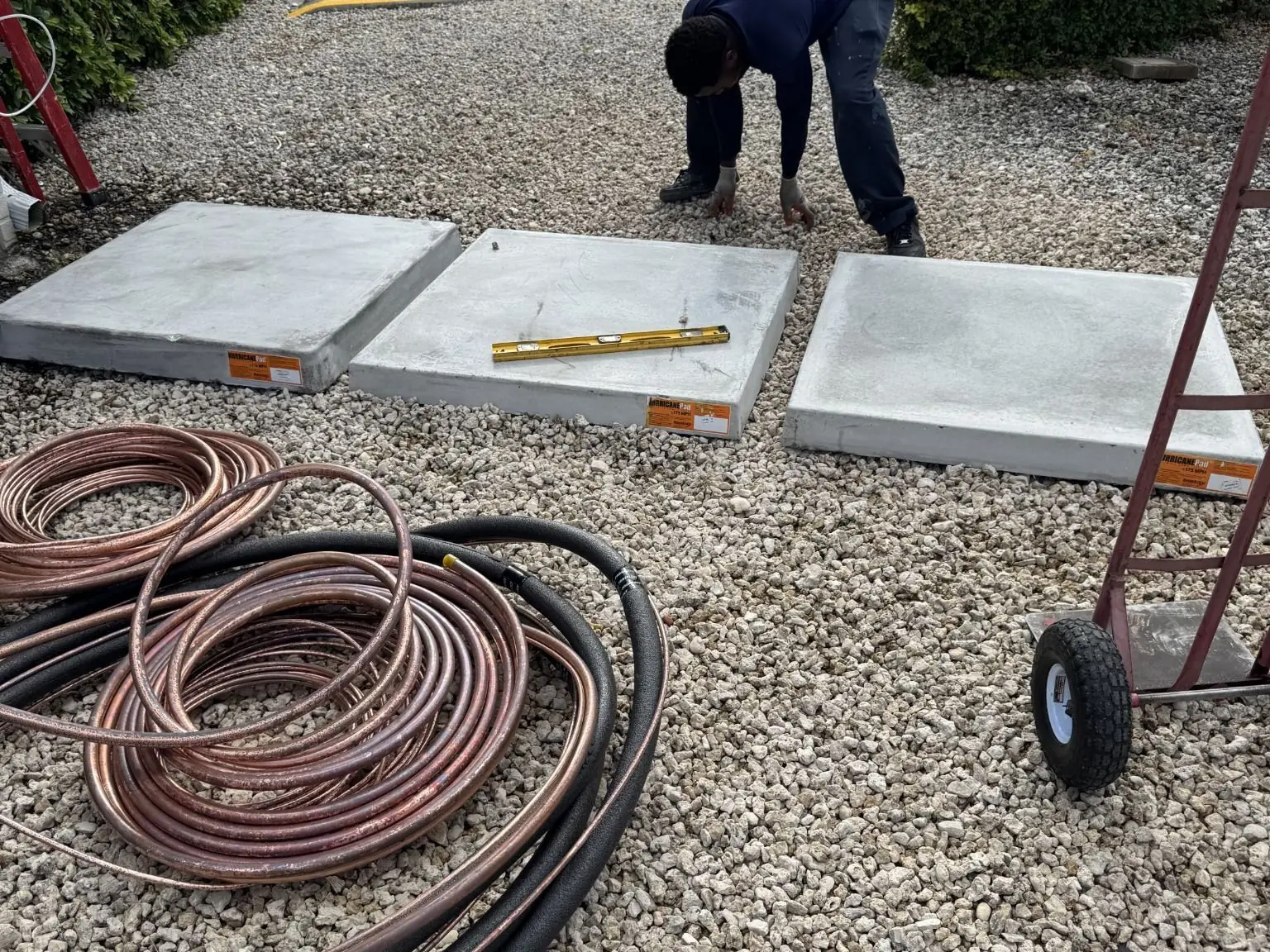 Leveling new equipment pads on gravel during an installation, with coils of refrigerant line set nearby