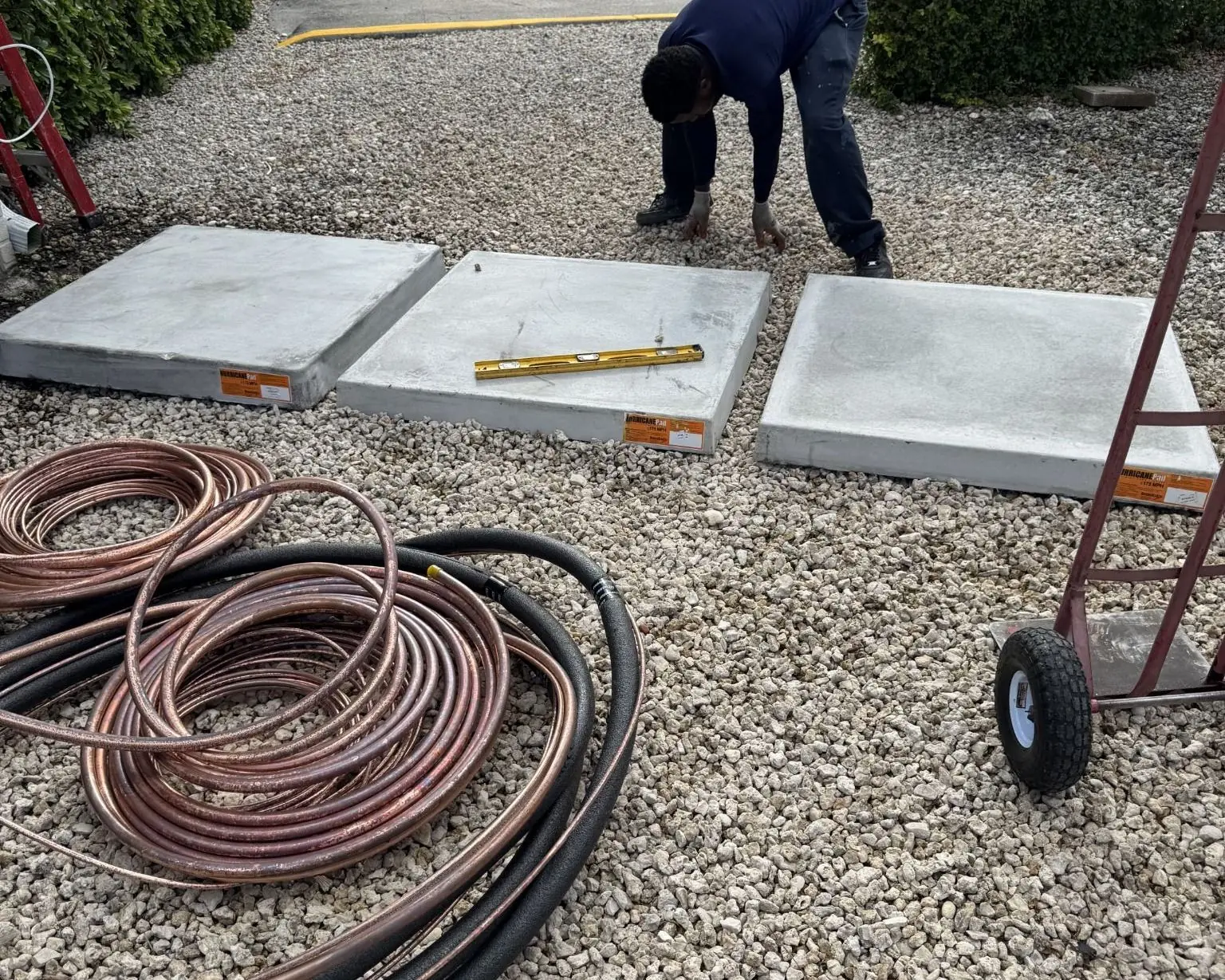 Leveling new equipment pads on gravel during an installation, with coils of refrigerant line set nearby