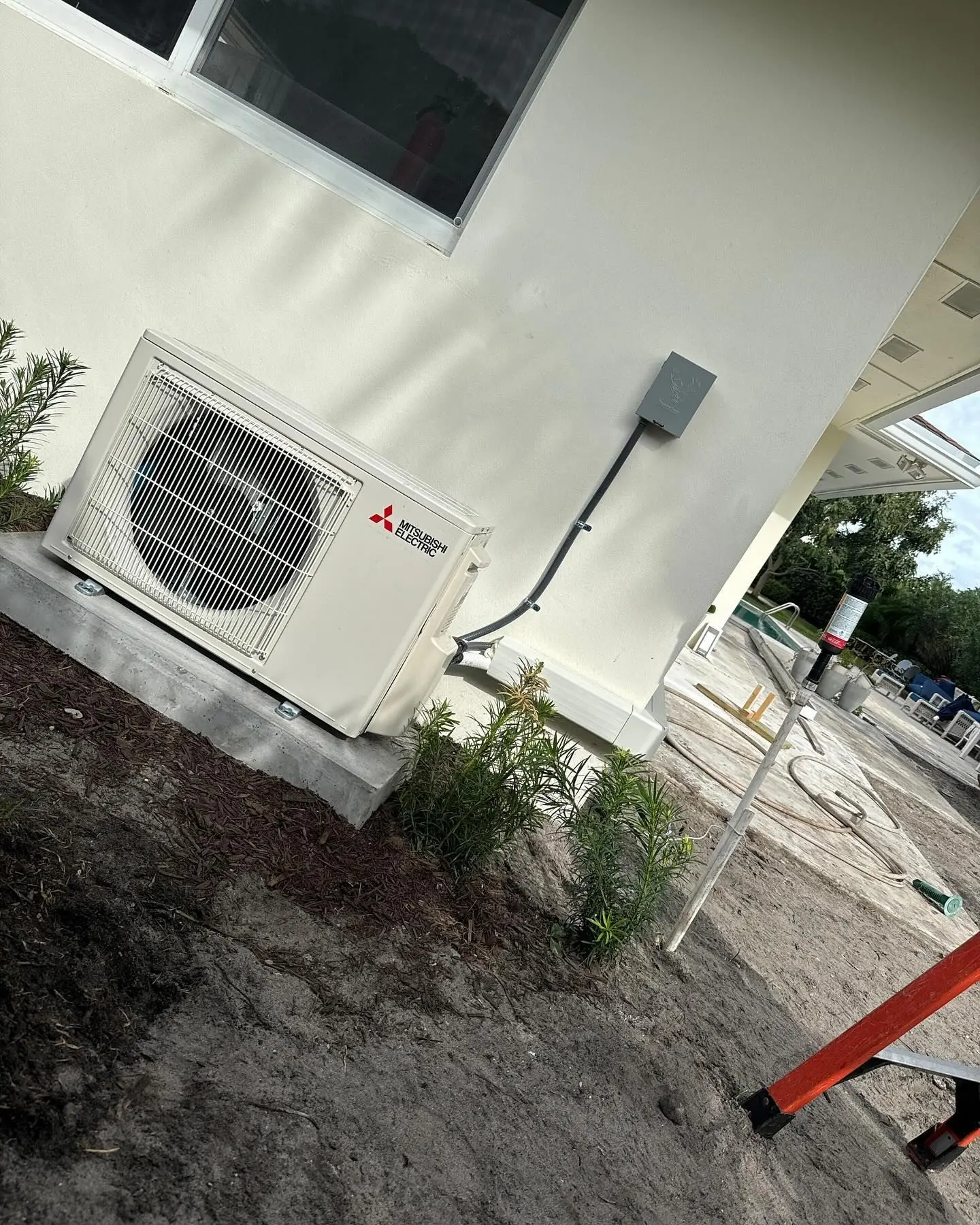 Mitsubishi Electric ductless mini-split outdoor unit on a pad against the wall of a newly built home