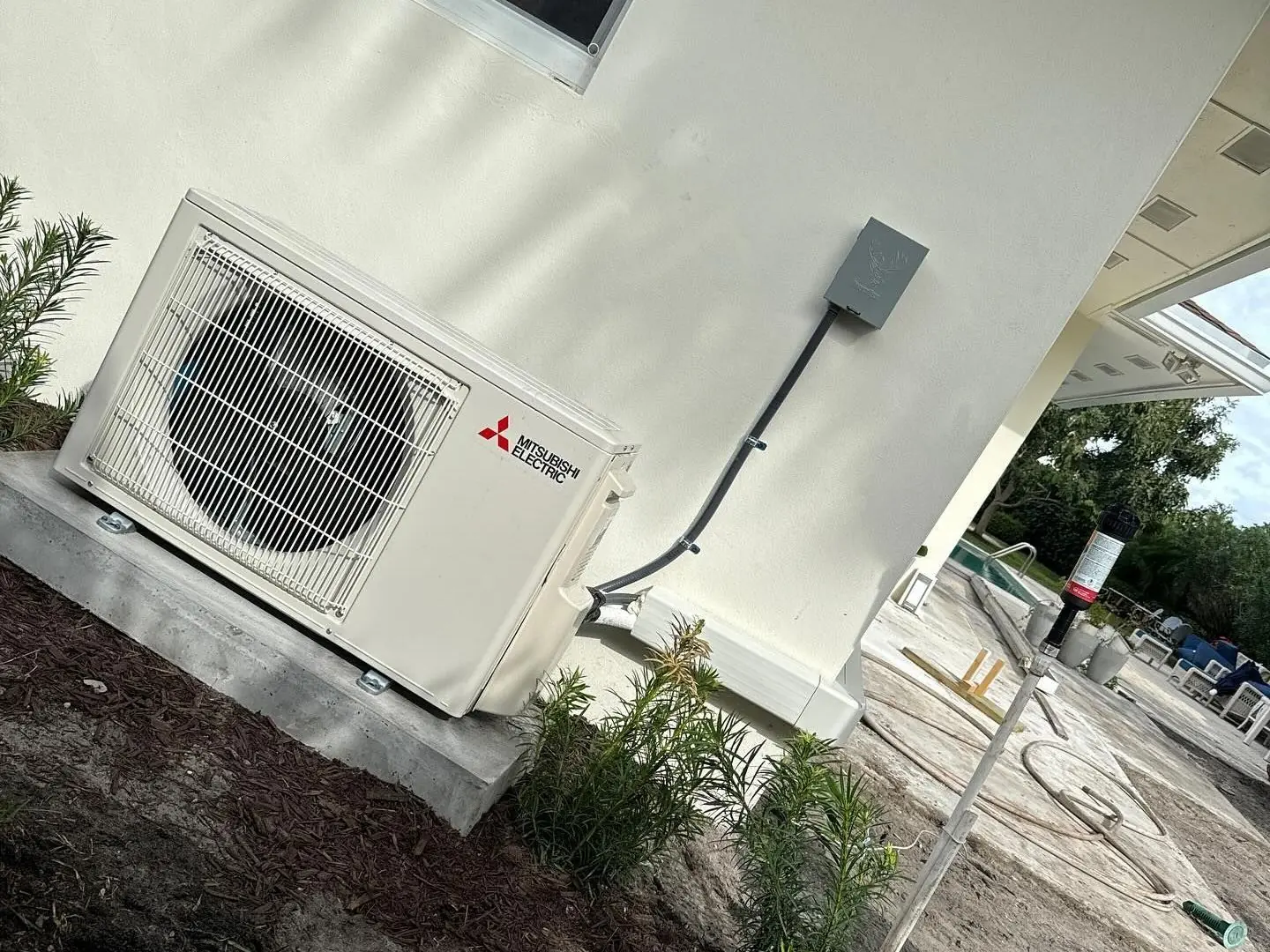 Mitsubishi Electric ductless mini-split outdoor unit on a pad against the wall of a newly built home
