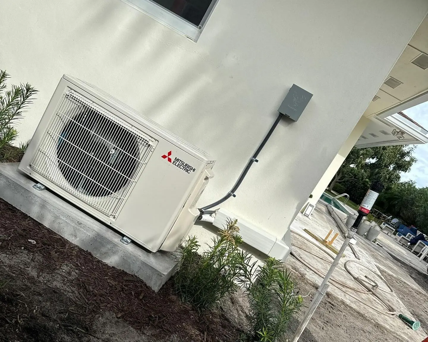 Mitsubishi Electric ductless mini-split outdoor unit on a pad against the wall of a newly built home