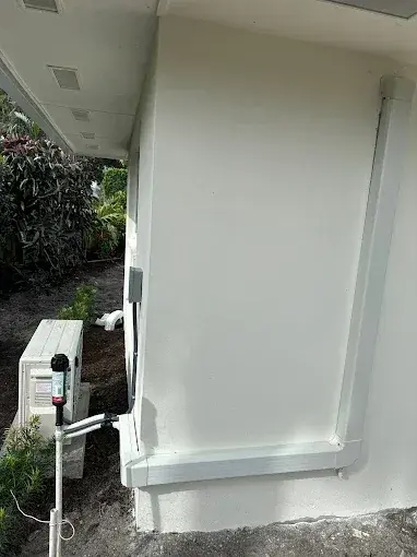 Mini-split outdoor unit beside a house, with the refrigerant lines run up the wall in a cover