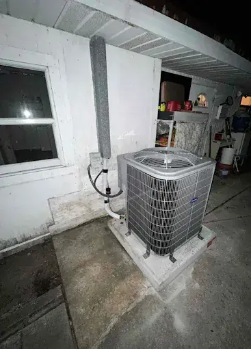 New condensing unit on its pad beside a house at night