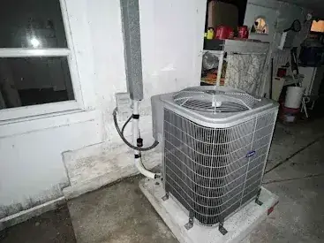New condensing unit on its pad beside a house at night