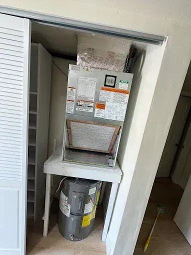 Air handler on a stand in a closet above the water heater, with the return filter in place
