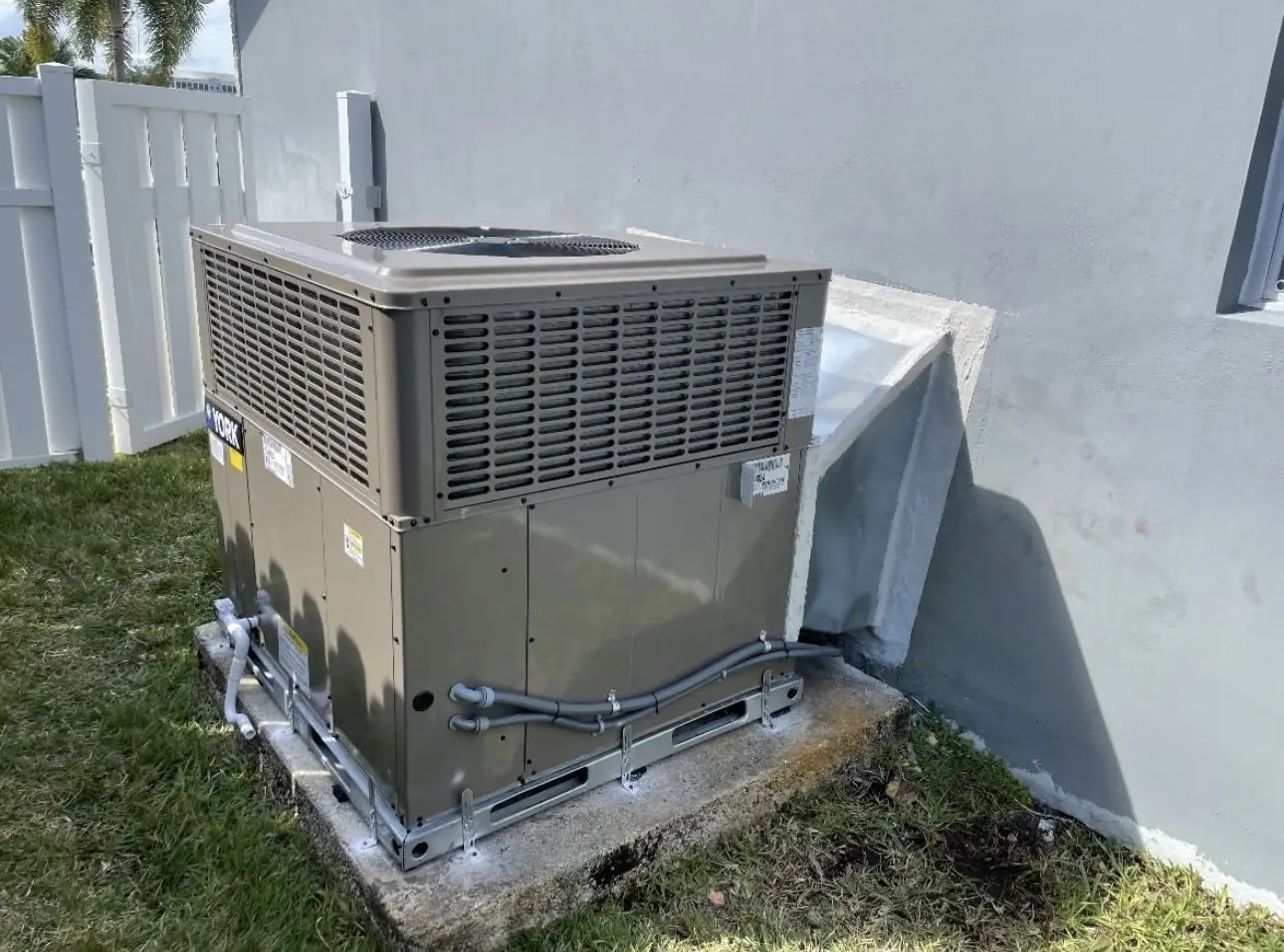 Packaged AC unit installed on a concrete pad with metal tie-down brackets