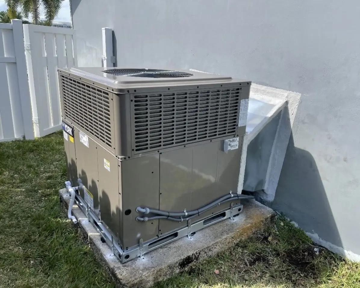 Packaged AC unit installed on a concrete pad with metal tie-down brackets