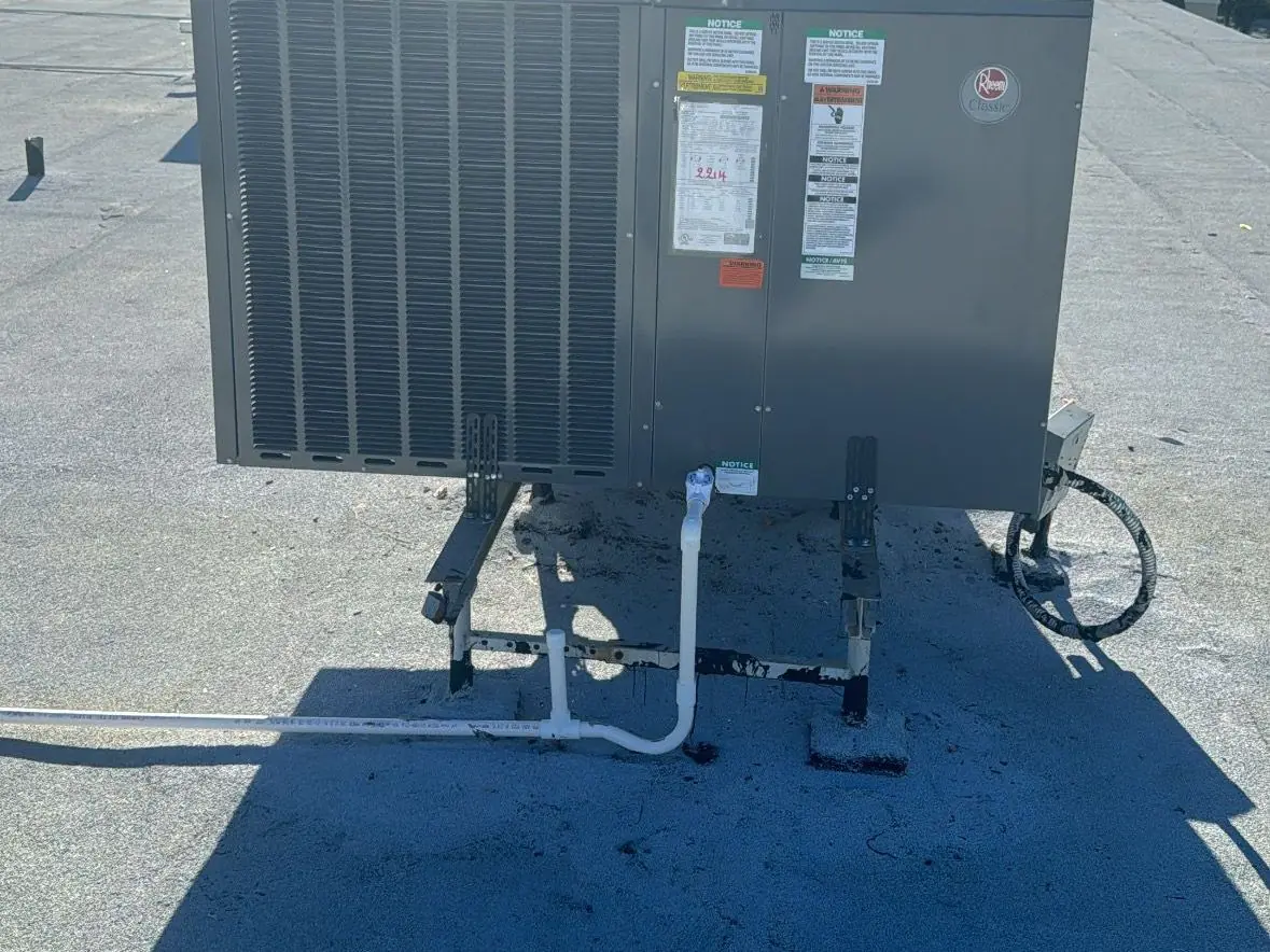 Rooftop packaged AC unit on a flat roof with palm trees in the distance