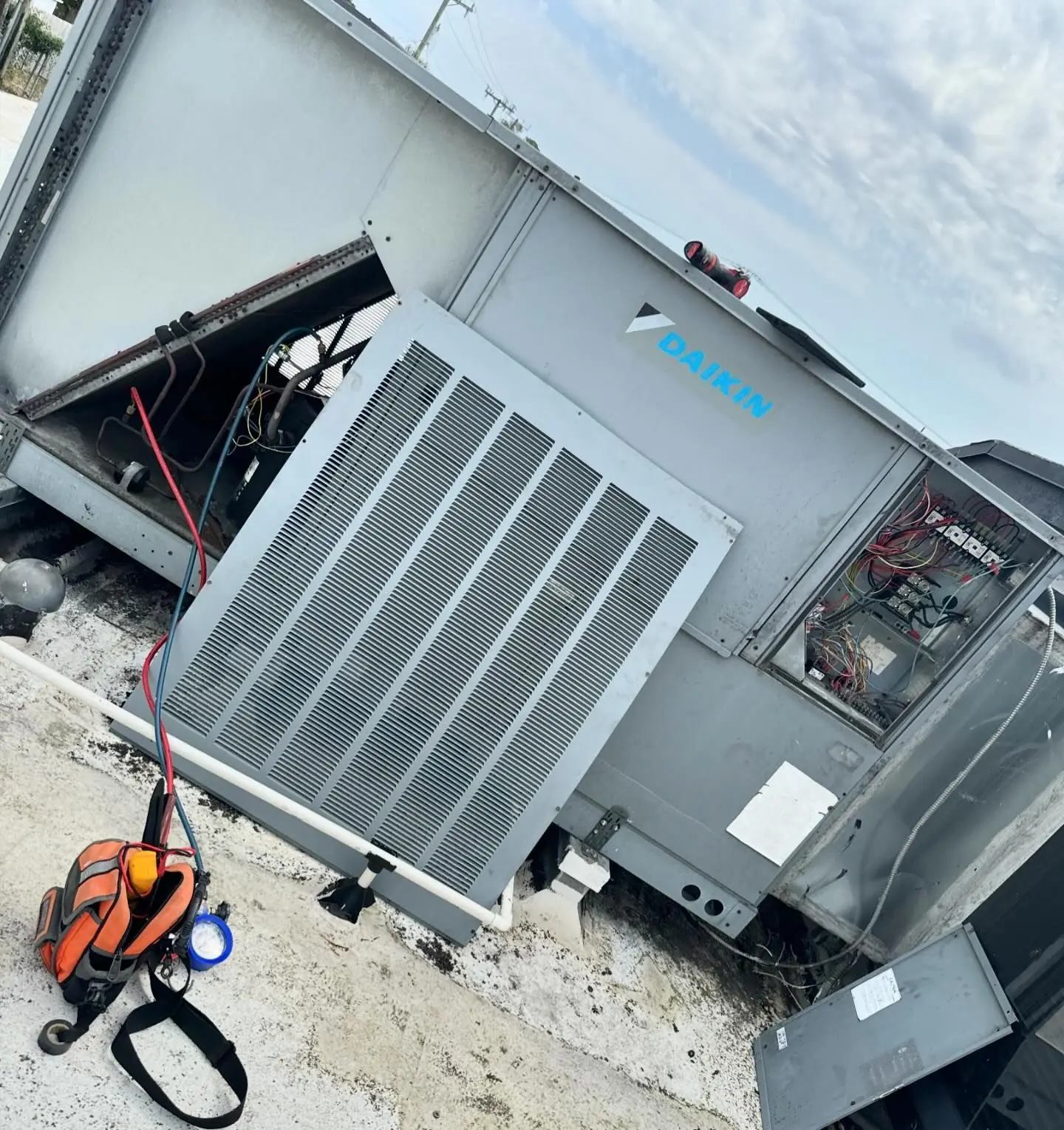Daikin rooftop packaged unit with its service panels open and refrigerant hoses connected, on a flat commercial roof