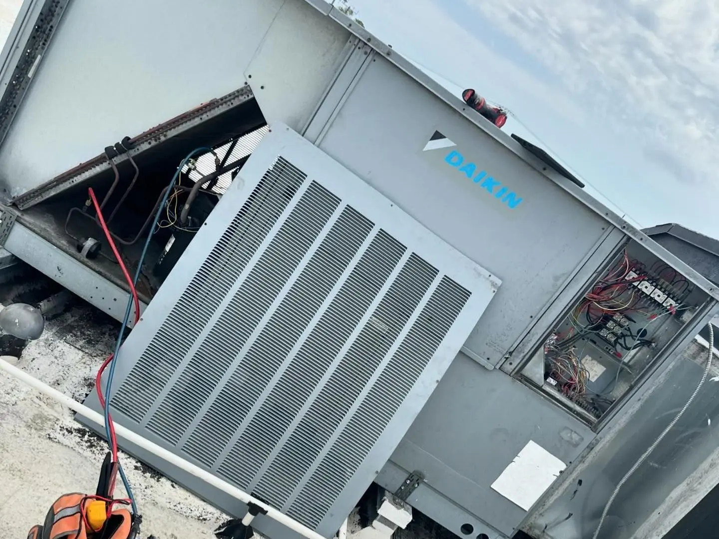 Daikin rooftop packaged unit with its service panels open and refrigerant hoses connected, on a flat commercial roof