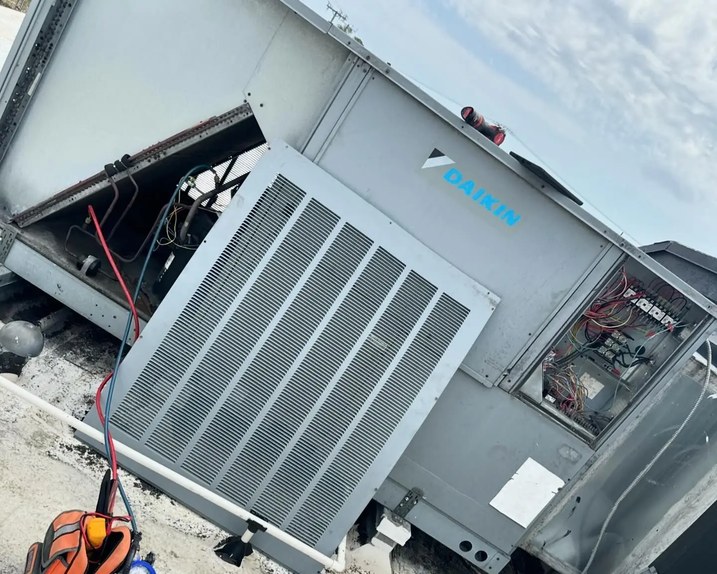 Daikin rooftop packaged unit with its service panels open and refrigerant hoses connected, on a flat commercial roof