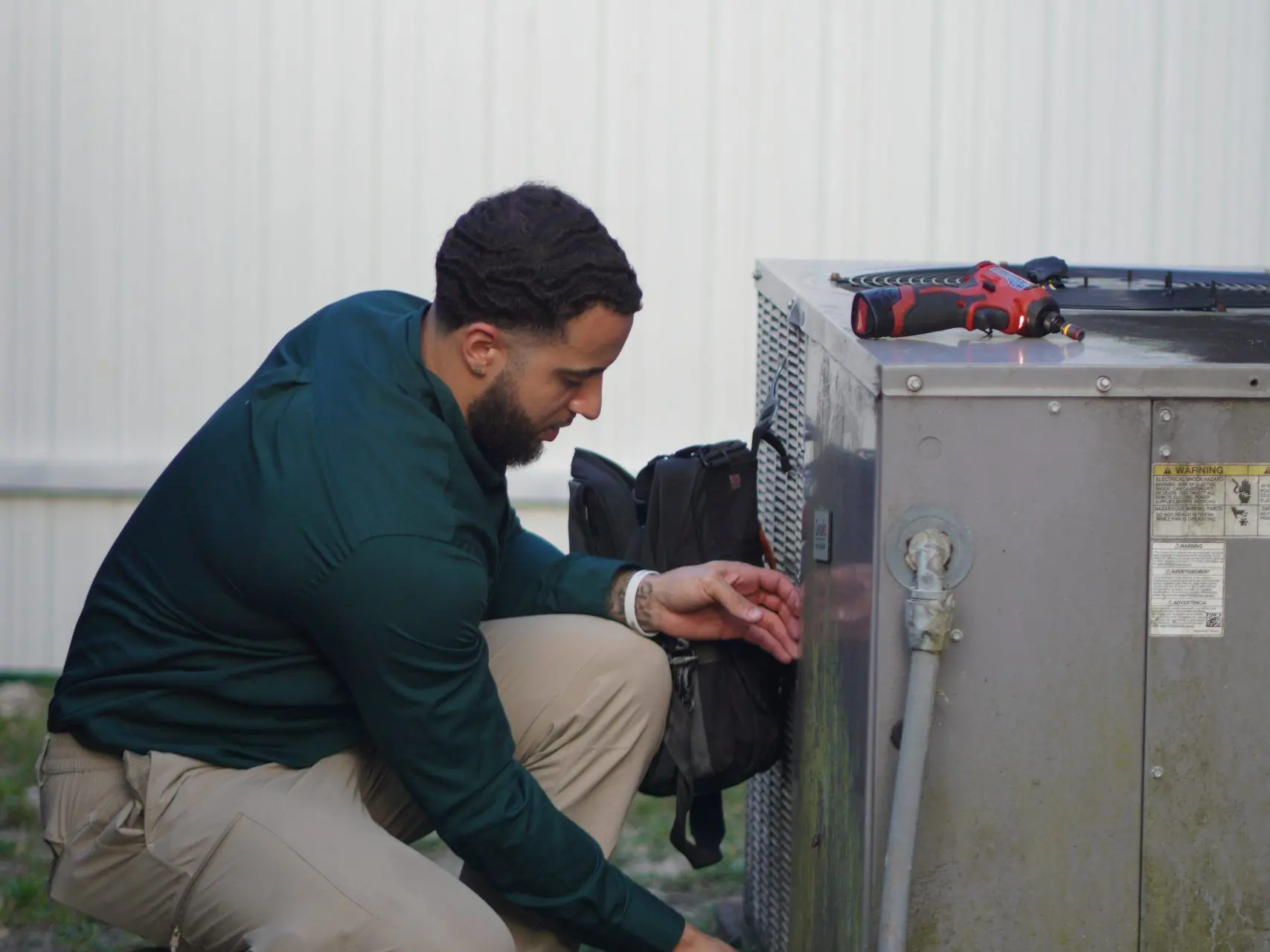 Service Shield technician kneeling at an outdoor unit, reaching into the service panel