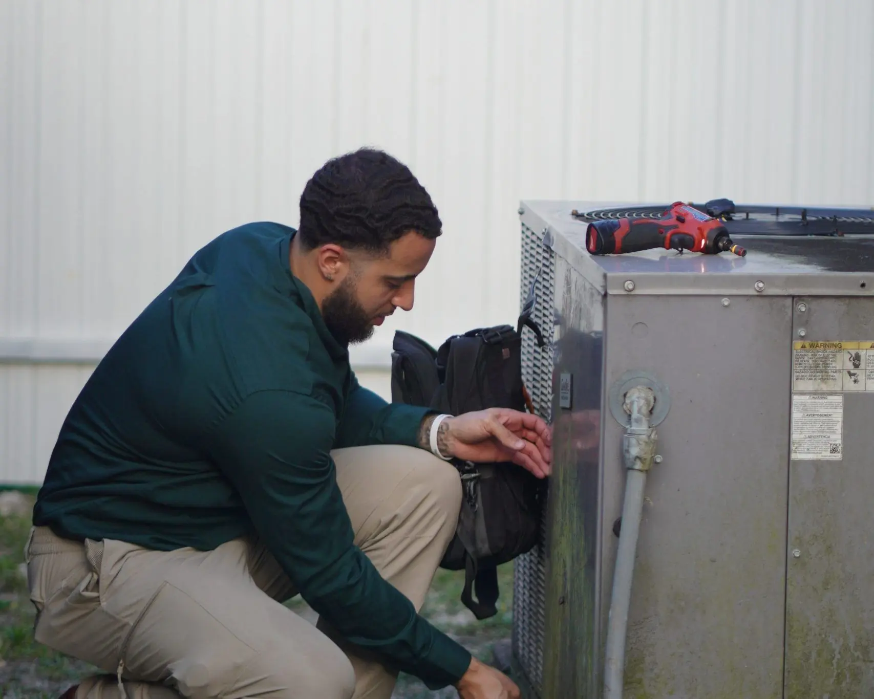 Service Shield technician kneeling at an outdoor unit, reaching into the service panel