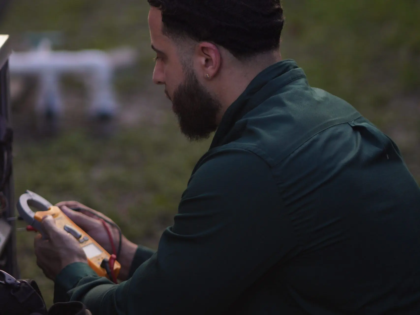 Close-up of a technician holding a clamp meter while testing an outdoor unit