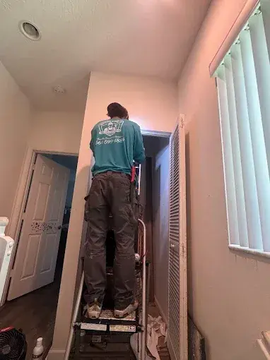 Service Shield technician on a ladder working at the top of an air handler closet