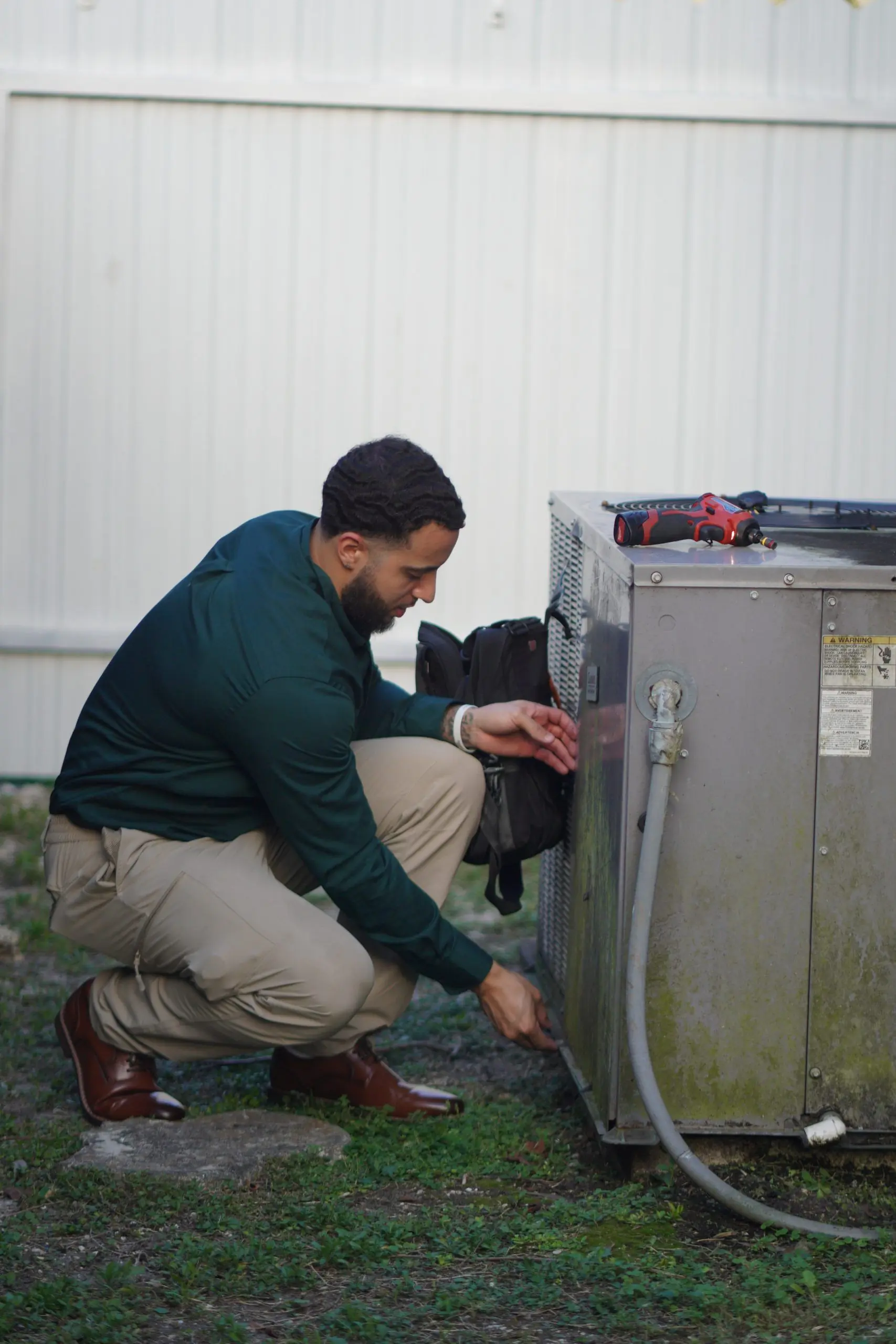 Technician crouched beside an outdoor condenser, removing its electrical service panel