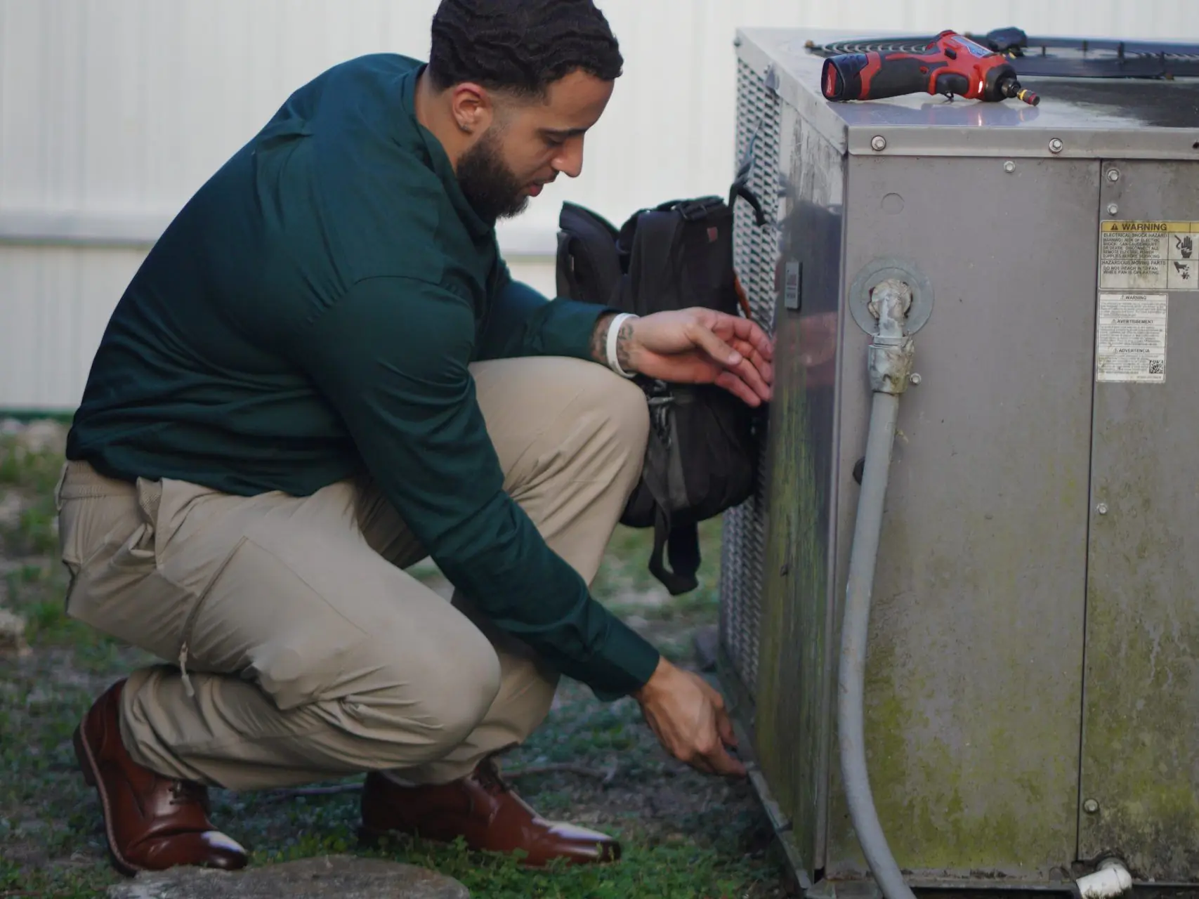 Technician crouched beside an outdoor condenser, removing its electrical service panel