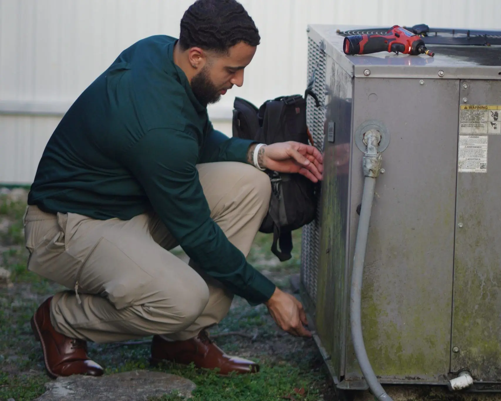 Technician crouched beside an outdoor condenser, removing its electrical service panel
