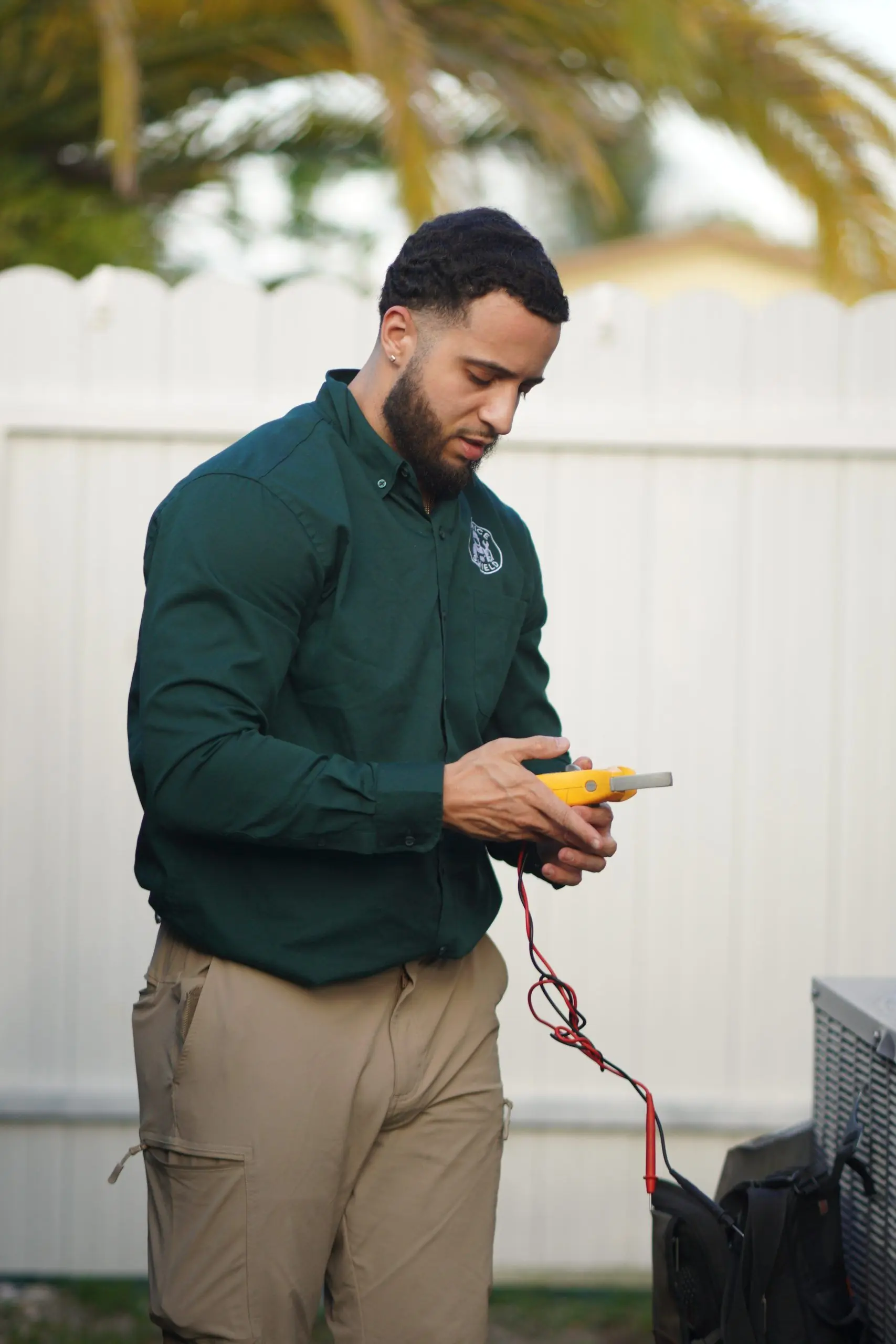 Technician standing in a backyard reading a digital multimeter with its test leads connected