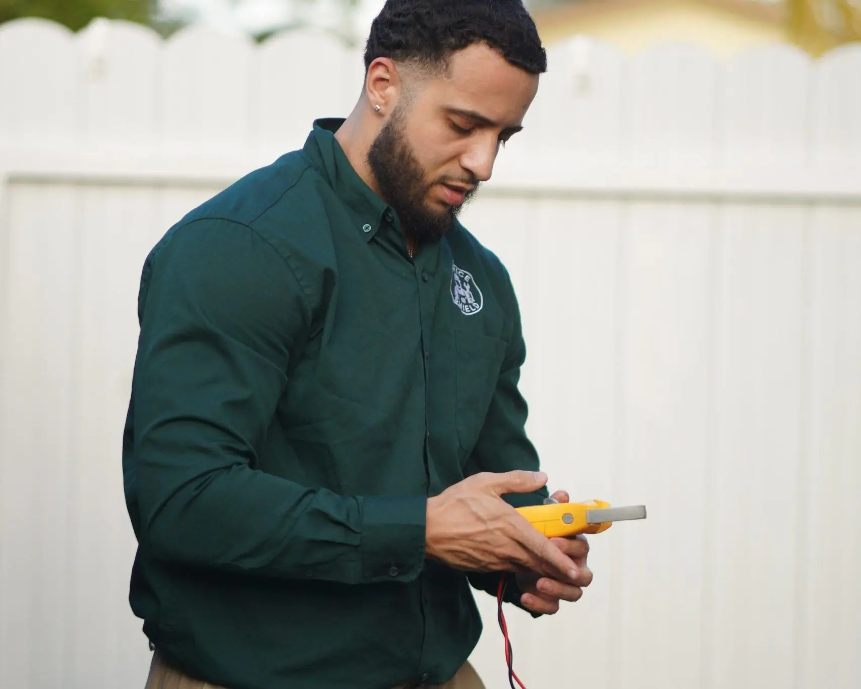 Technician standing in a backyard reading a digital multimeter with its test leads connected