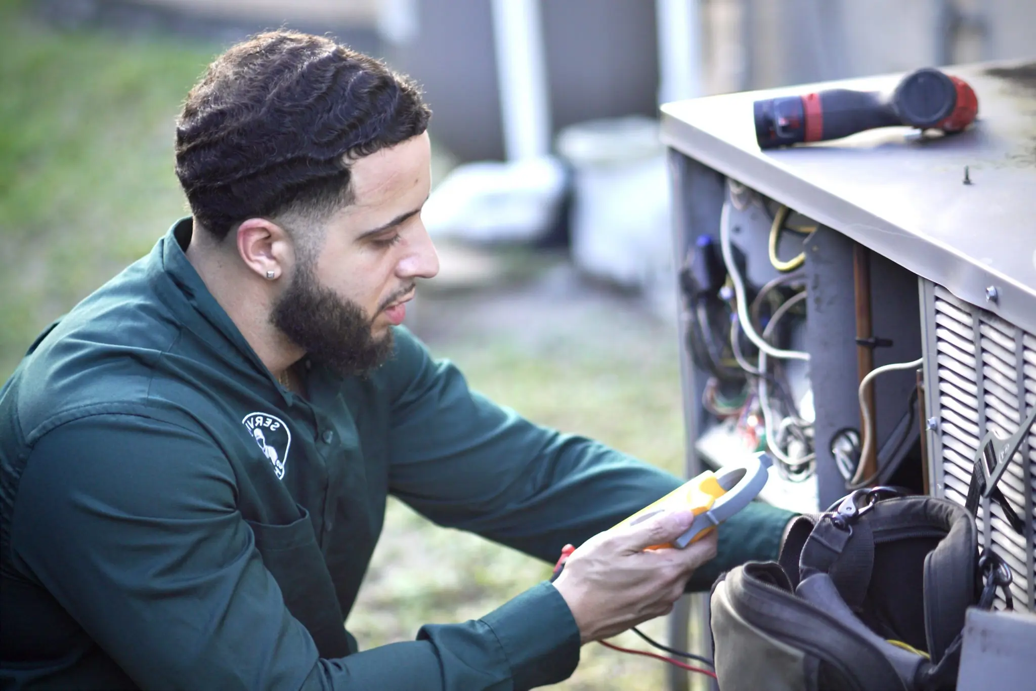 Service Shield technician using a clamp meter on the electrical compartment of an outdoor AC condenser
