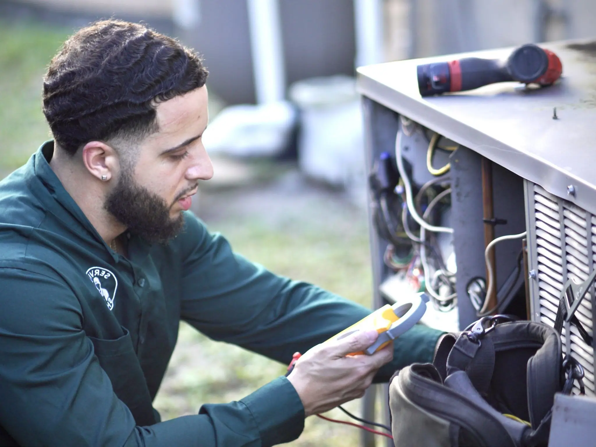 Service Shield technician using a clamp meter on the electrical compartment of an outdoor AC condenser